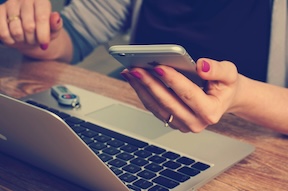 Close-up of a pair of hands using a phone beside a computer